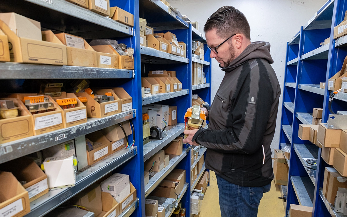 Ein Mitarbeiter steht vor einem Regal mit und betrachtet ein Bauteil